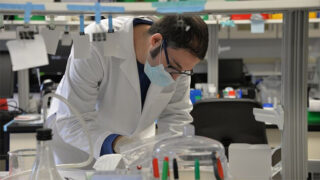 Jeremy Logue, PhD, bent over a desk in a lab taking notes