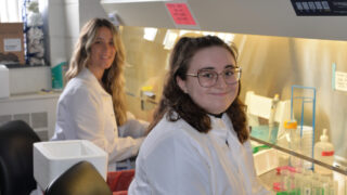 Two researchers smile in front of equipment in the lab of researchers Kate MacNamara