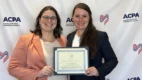 Two women stand holding a certificate with an American Cleft Palate Craniofacial Association step-and-repeat as the backdrop