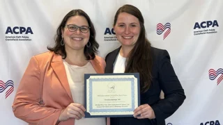 Two women stand holding a certificate with an American Cleft Palate Craniofacial Association step-and-repeat as the backdrop