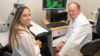 Scientists Whitney Longmate, PhD, and Michael DiPersio, PhD, wearing white coats and sitting near a computer with a green and red image