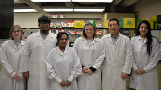 Six scientists in white coats standing together in Dr. Wei Sun's research lab