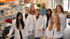 Group of eight basic science researchers, including Sophie Belin, PhD, and Yannick Poitelon, PhD, stand together in a laboratory