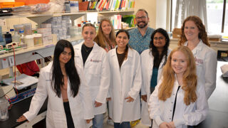 Group of eight basic science researchers, including Sophie Belin, PhD, and Yannick Poitelon, PhD, stand together in a laboratory