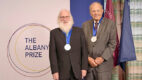 The two recipients of the 2026 Albany Medical Center Prize in Medicine and Biomedical Research standing near the Albany Prize logo wearing their Prize medals