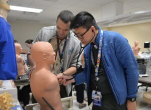 Two pediatric residents practice listening to a patient's heart using a mannequin.