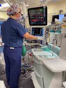 A Certified Registered Nurse Anesthesiologist (CRNA) using equipment in an operating room.