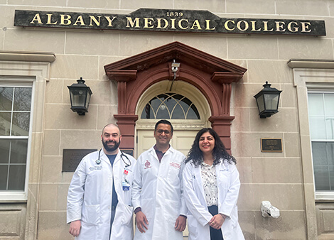 Three doctors in white coats stand outside the Albany Medical College entrance