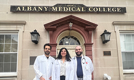 Three people in white coats stand outside Albany Medical College