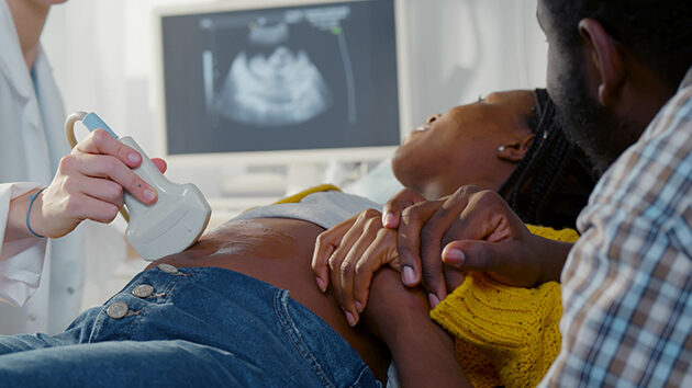 A pregnant woman is getting an ultrasound. She and her husband are looking at the monitor