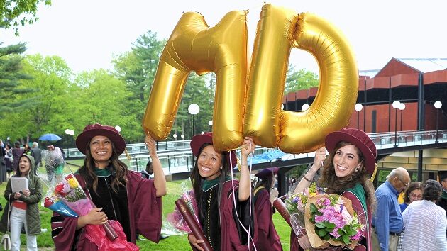 Three graduates holding gold letter balloons that say "M.D."