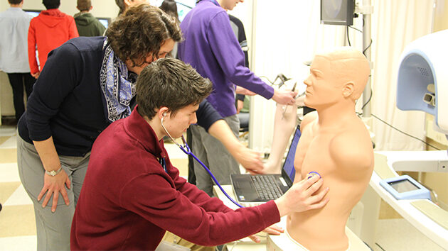 A student receives guidance from an instructor on listening for a heartbeat with a stethoscope.