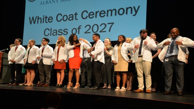 First-year medical students stand in a line on a stage, to put on their white coats for the first time, in the White Coat Ceremony
