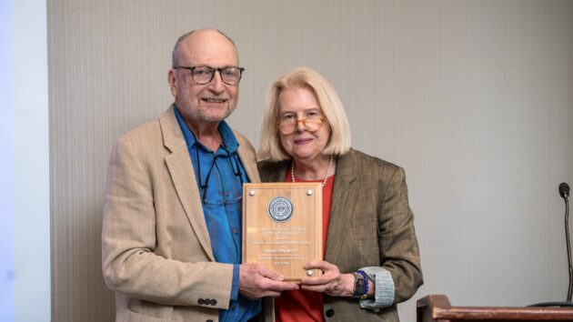 A woman presents an award to a man. The two smile and pose for a picture.