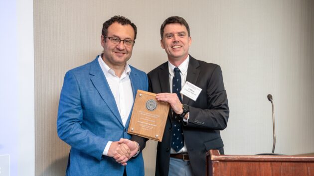 A man presents an award to another man. The two smile and pose for a picture.