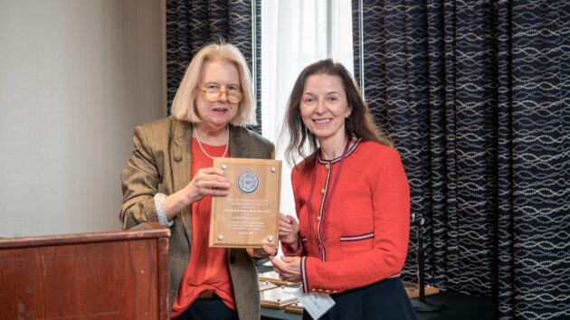 A woman presents an award to another woman. The two smile and pose for a picture.