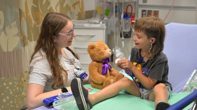 A child life specialist explains a procedure to a peds patient with a teddy bear