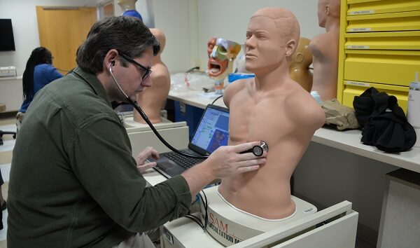 A pediatric resident practices listening to a patient's heart using a mannequin.