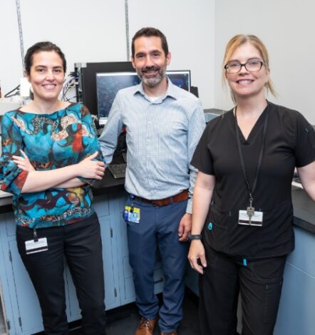 Three members of the Department of Pathology at Albany Medical Center stand in front of machinery used to analyze blood samples